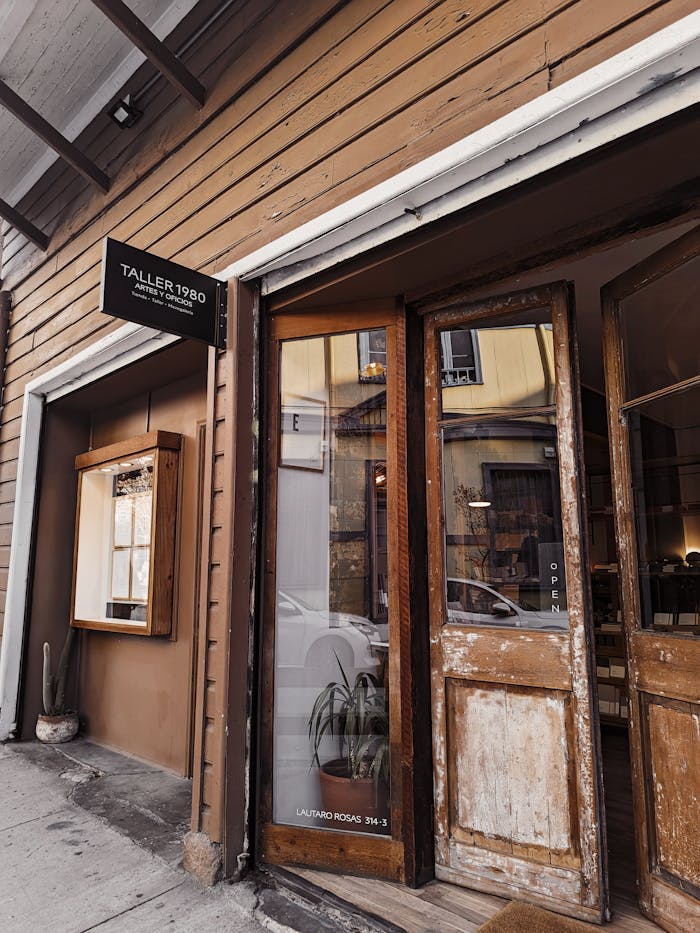 Rustic wooden workshop entrance with open sign, vintage charm, and glass door reflecting street view.